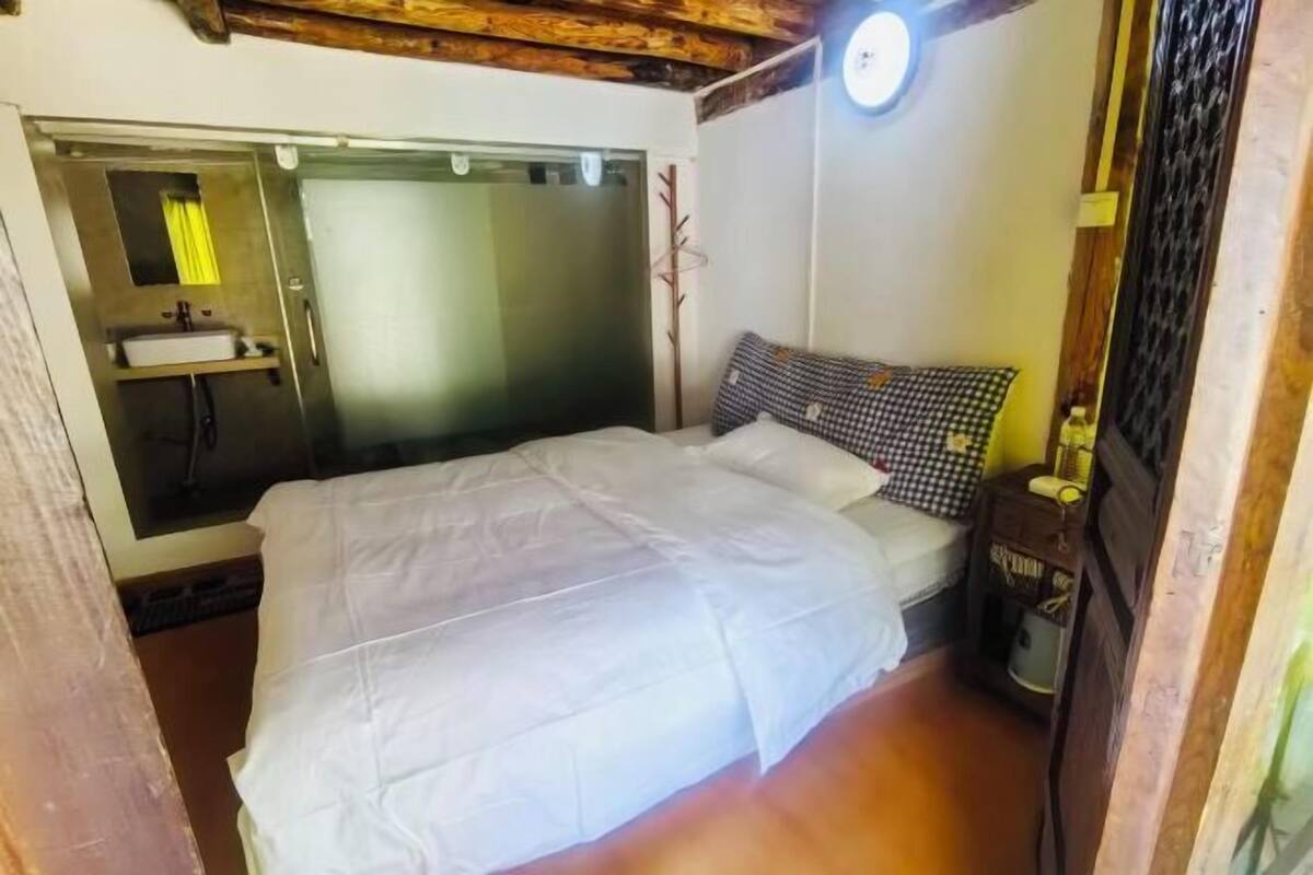 Un dormitorio con cama, mesita de noche, espejo y ventana.