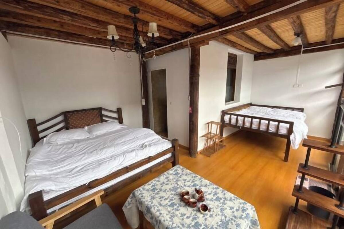 Una habitación con dos camas de madera, una mesita con mantel floreado y una silla de madera.