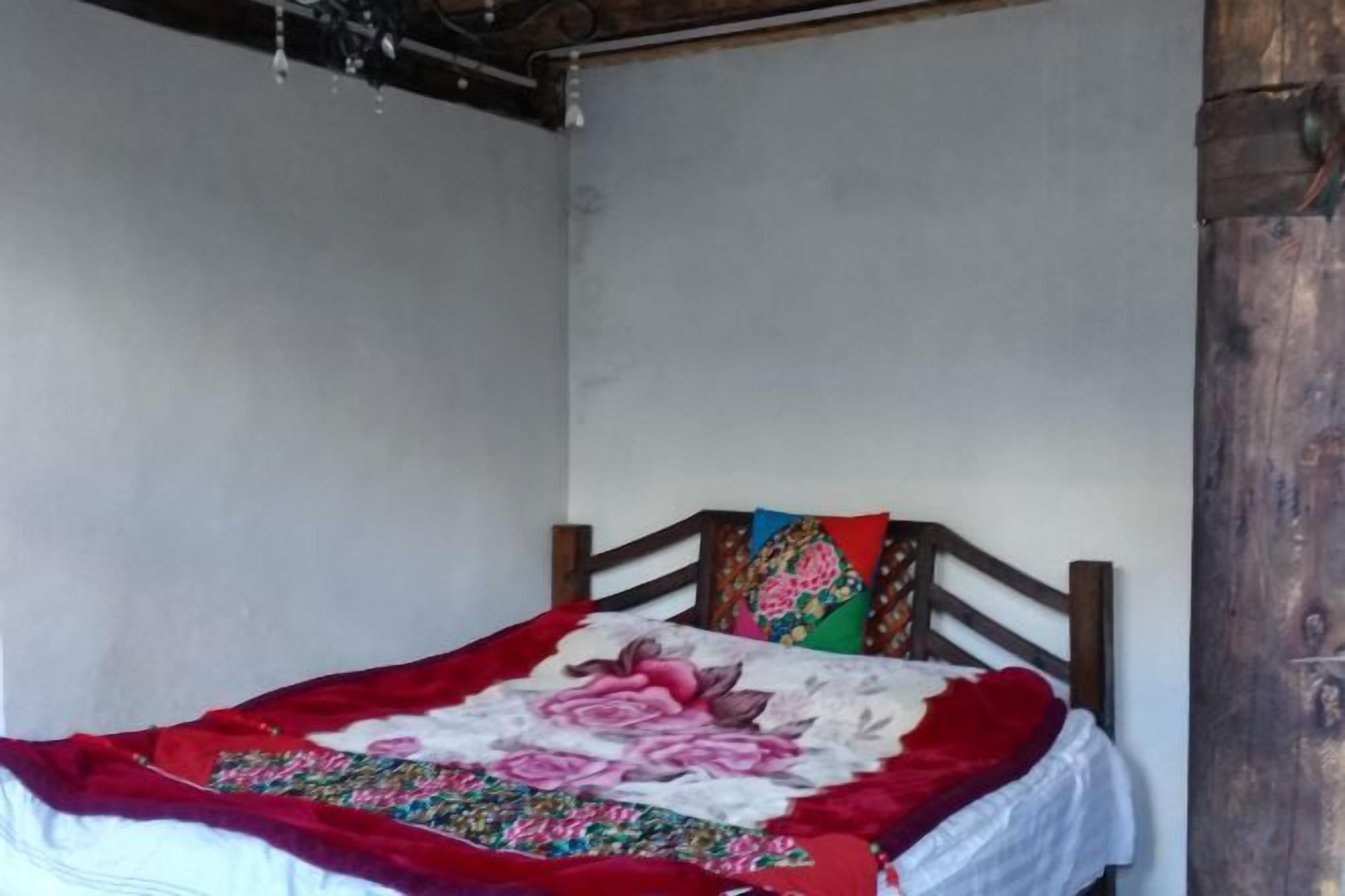 A single bed with a wooden headboard, a floral-patterned bedspread, and a red blanket.