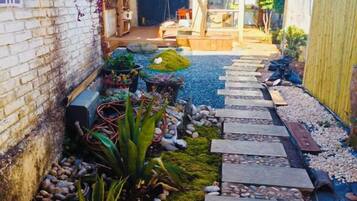 A narrow stone pathway leading to a wooden door, surrounded by potted plants and a small garden area.