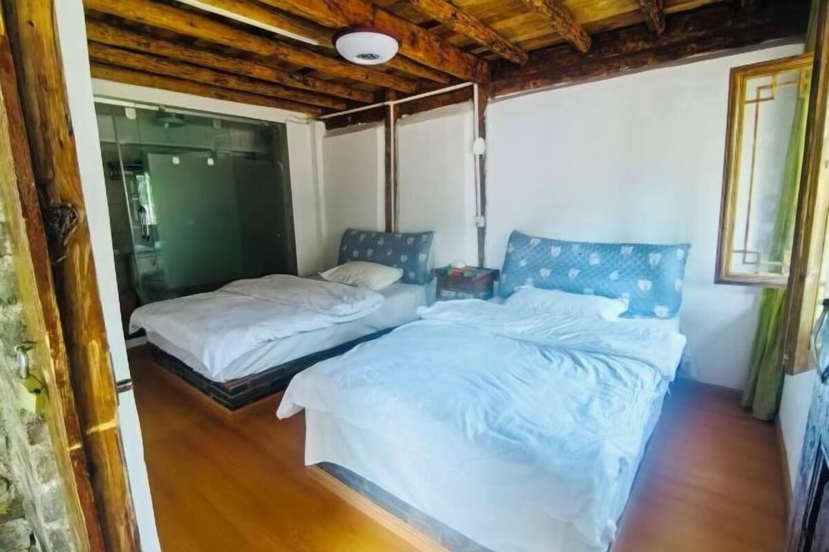 Una habitación con techo de madera, una cama con ropa blanca, una mesita de noche y una ventana con cortina.