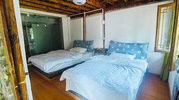A room with a wooden ceiling, a bed with white bedding, a bedside table, and a window with a curtain.