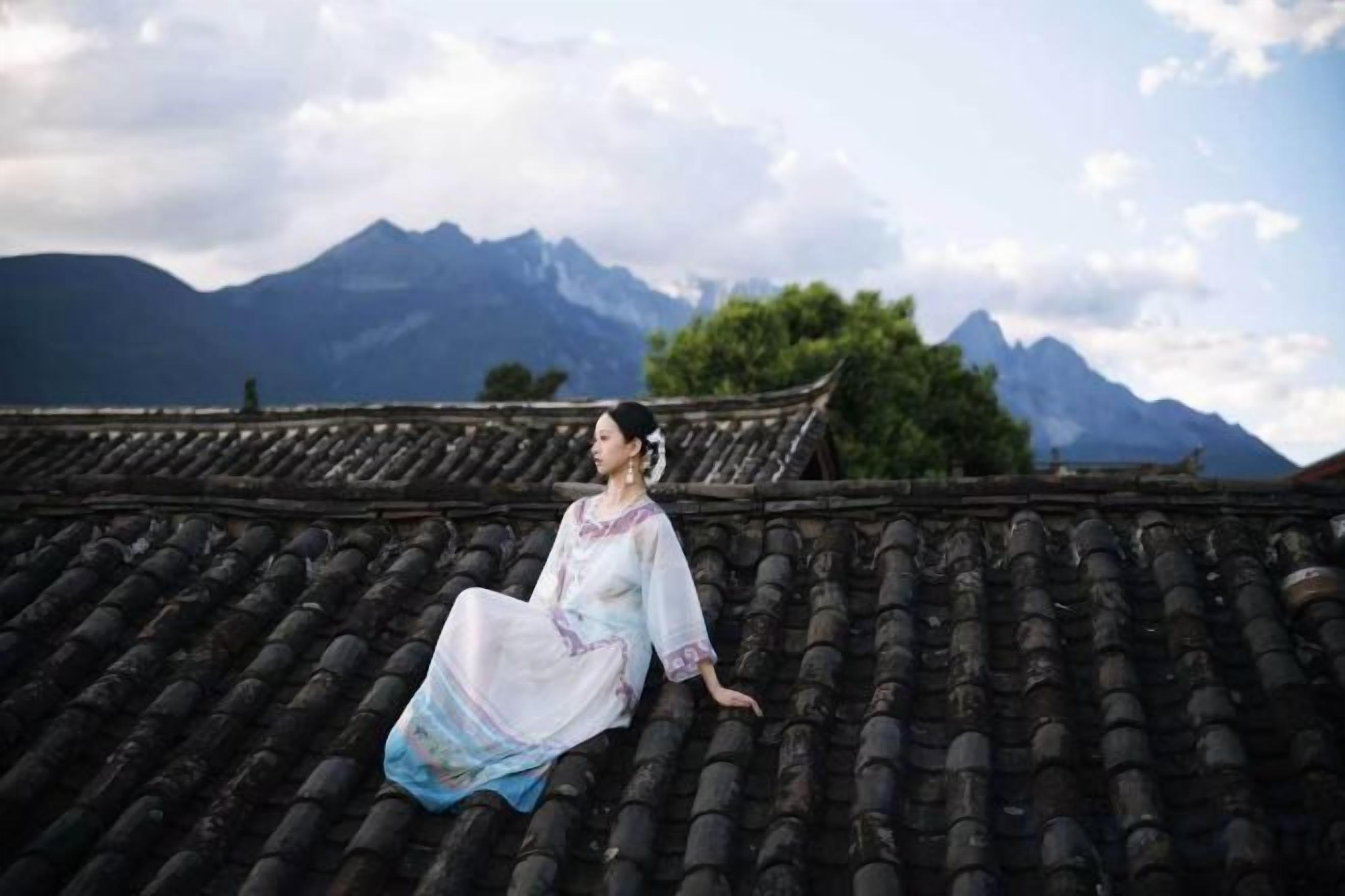 A person sitting on a traditional tiled roof with mountains in the background.