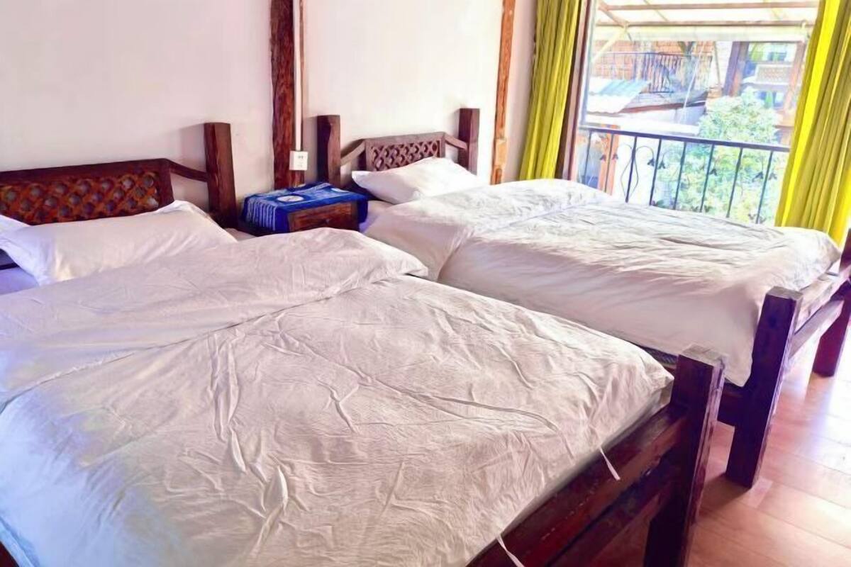 Una habitación con dos camas de madera, una mesita y un balcón con cortinas amarillas.