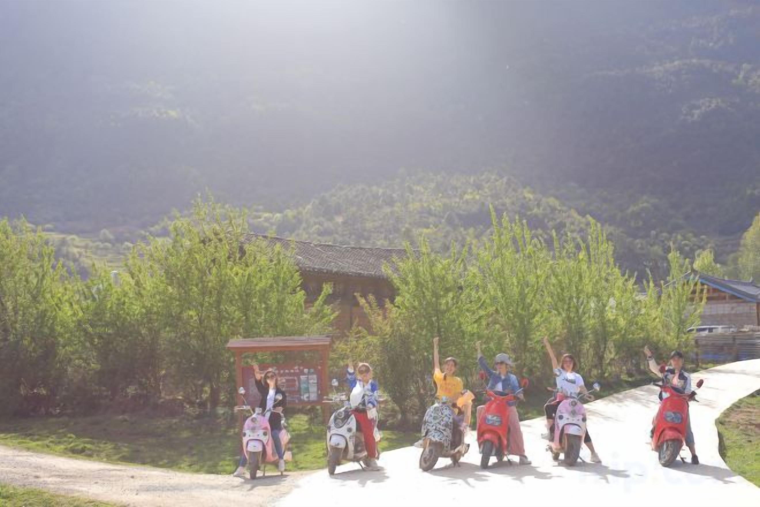 Un grupo de personas en scooters en un entorno rural, con un edificio tradicional y vegetación de fondo.