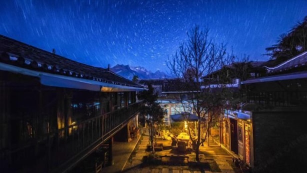 A courtyard with a starry night sky, traditional architecture, and a pathway leading to a building. - Leisure Inn Lijiang (Yulong)