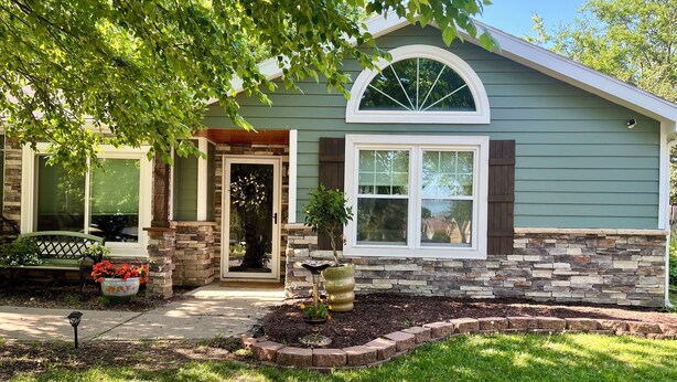 A house with a stone facade, a front door with a glass panel, and a small garden with a bench and potted plants.