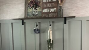 A wall with a sign stating 'THIS HOME IS FILLED WITH LOVE & LAUGHTER,' a framed picture, and two macramé hangings.