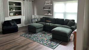 A living room with a sectional sofa, a fireplace, a small table, and a view of the outdoors.
