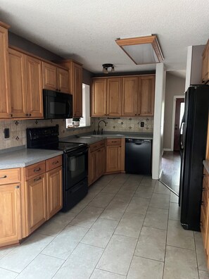 A kitchen with wooden cabinets, a microwave, stove, dishwasher, and a refrigerator. - 3-bedroom house in gorgeous Lawrence with easy access to K-10 and I-70 (Lawrence)