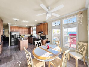 A kitchen with wooden cabinets, a refrigerator, and a dining area with a round table and chairs. - It's A Shellabration 3 Bedroom Home (Port Bolivar)