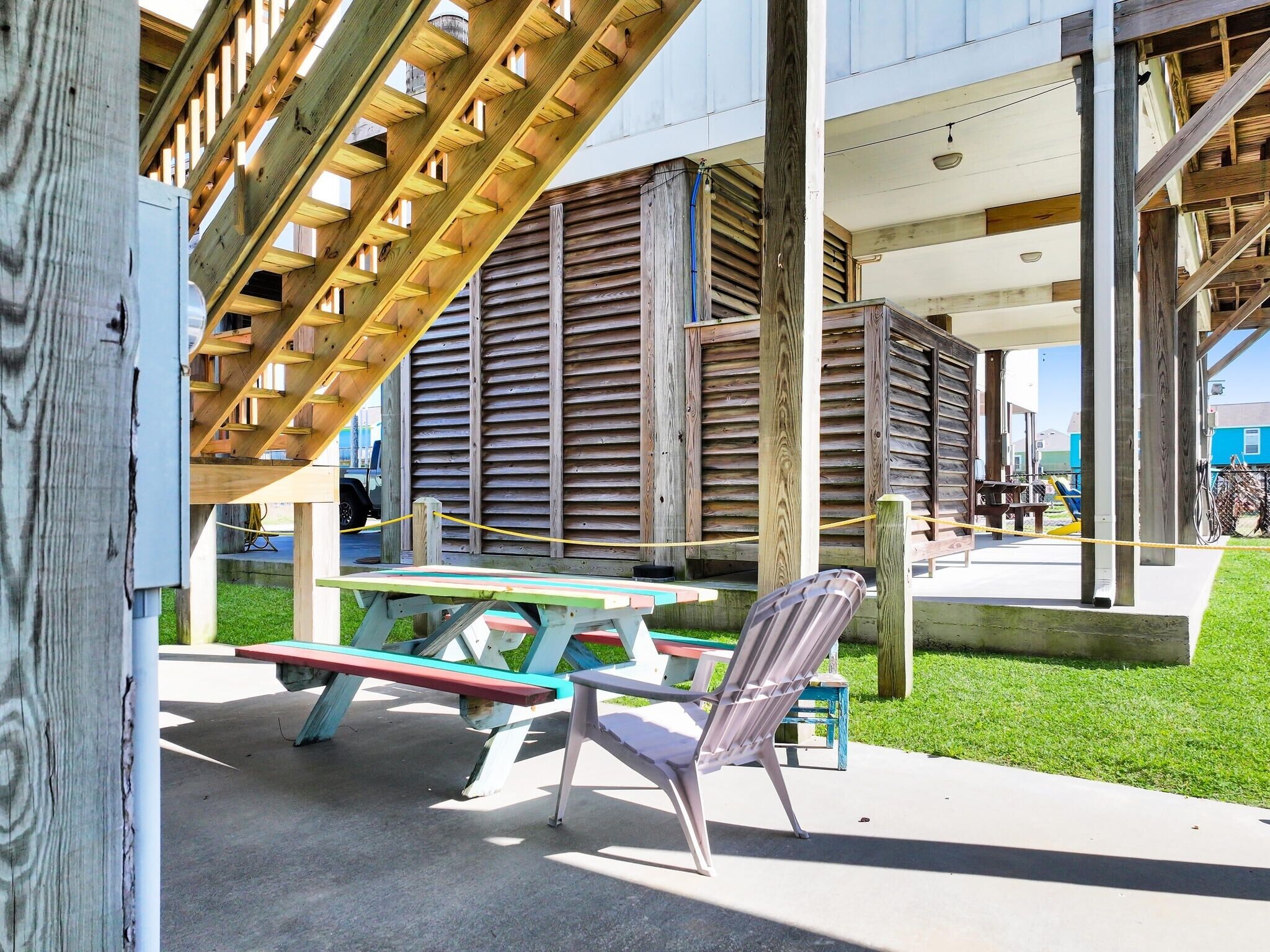 A wooden structure with a slatted roof, a picnic table, and a chair.