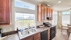 A kitchen with wooden cabinets, a double sink, a dishwasher, and a view of the neighborhood. - It's A Shellabration 3 Bedroom Home (Port Bolivar)