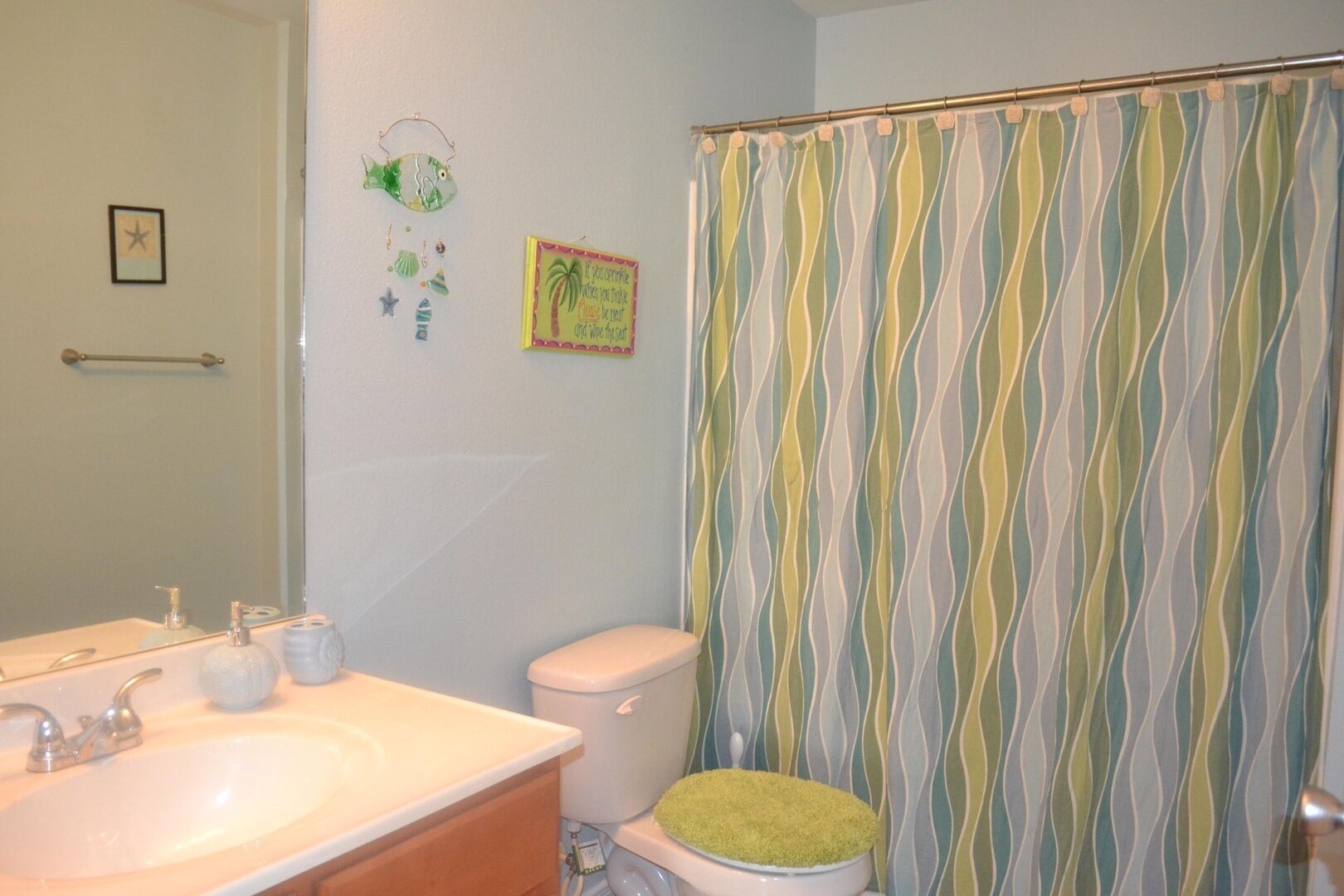 A bathroom with a white sink, a toilet with a green seat, a striped shower curtain, and a dreamcatcher decoration.
