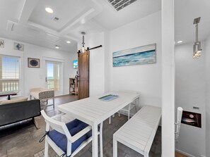 Ein modernes Interieur mit einem weißen Essbereich, einem schwarzen Sofa und Ausblick nach draußen.