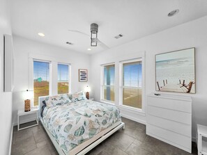 Ein Schlafzimmer mit Bett, Deckenventilator, Nachttisch, Lampe und einem Gemälde an der Wand.