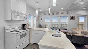 A modern kitchen with white cabinetry, a built-in oven, a large island with a sink, and pendant lighting. - Crystal By The Ocean 4 Bedroom Home (Port Bolivar)