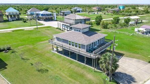 A residential area with a prominent house featuring a balcony, a covered deck, and a well-maintained lawn. - Amy's Dream 3 Bedroom Home (Port Bolivar)
