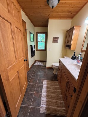 Een badkamer met toilet, wastafel, houten kastjes en een raam met jaloezieën.
