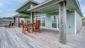 Eine Holzterrasse mit Tisch und Stühlen, einem überdachten Bereich und einem Gebäude mit Fenstern und einer Veranda.