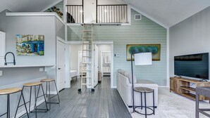 Ett loftliknande vardagsrum med en trappa, en tv och en matplats.