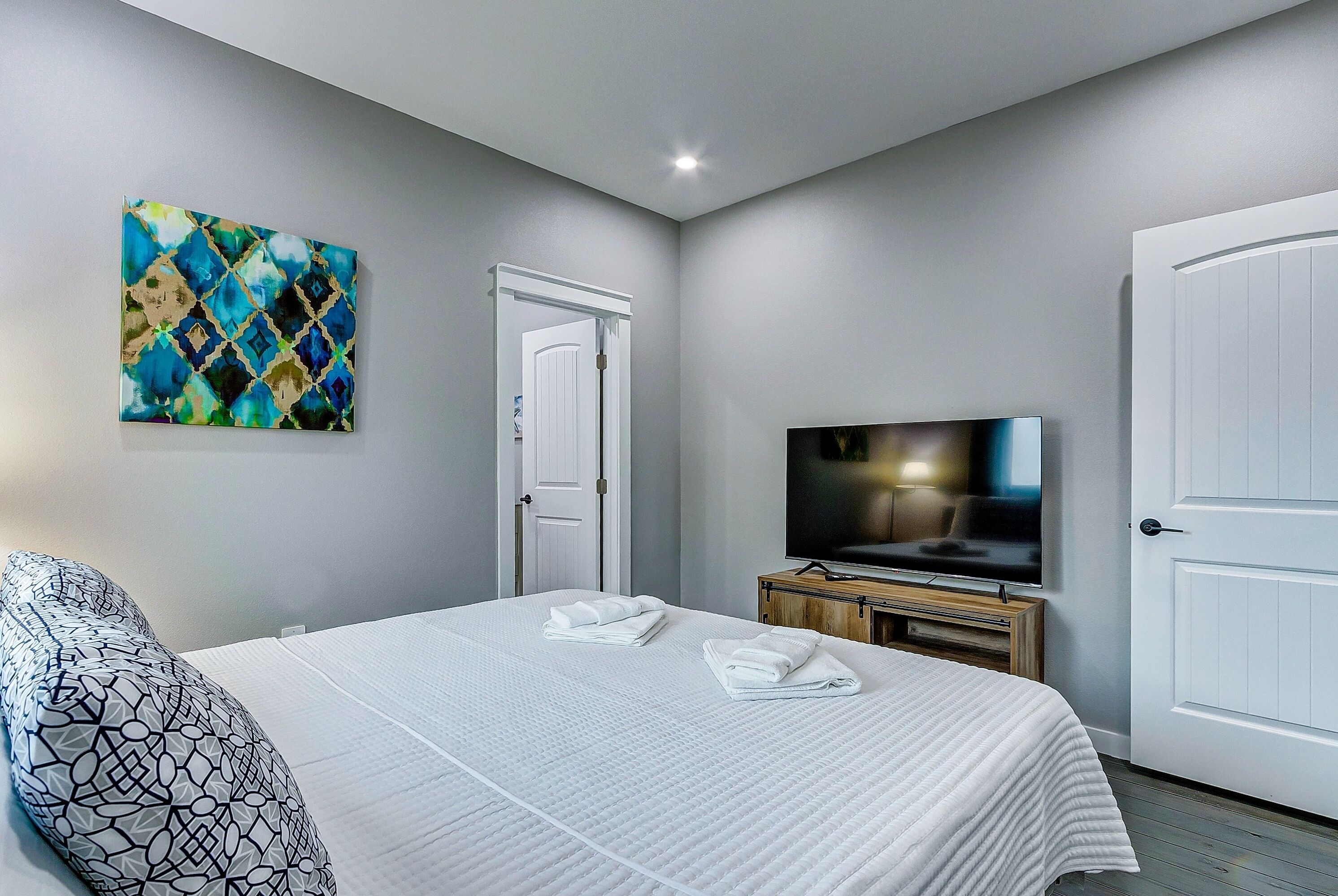 A bedroom with a bed, a TV, a door, and a painting on the wall.
