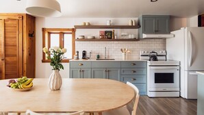 A kitchen with a round table, chairs, a vase with flowers, and a fruit bowl.