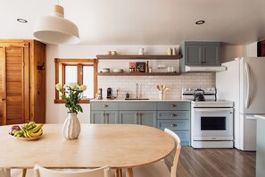 A kitchen with a round table, chairs, a vase with flowers, and a fruit bowl.