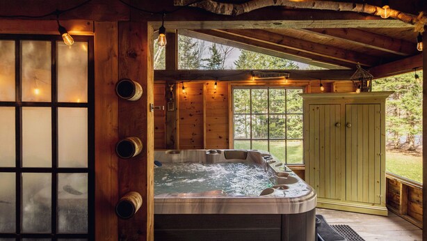 A wooden cabin with a hot tub, wooden walls, and a large window.