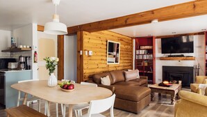 A cozy living room with a wooden ceiling, a fireplace, a television, and a dining area with a table and chairs.
