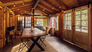 A rustic wooden cabin interior with a large dining table, wooden walls, and large windows.