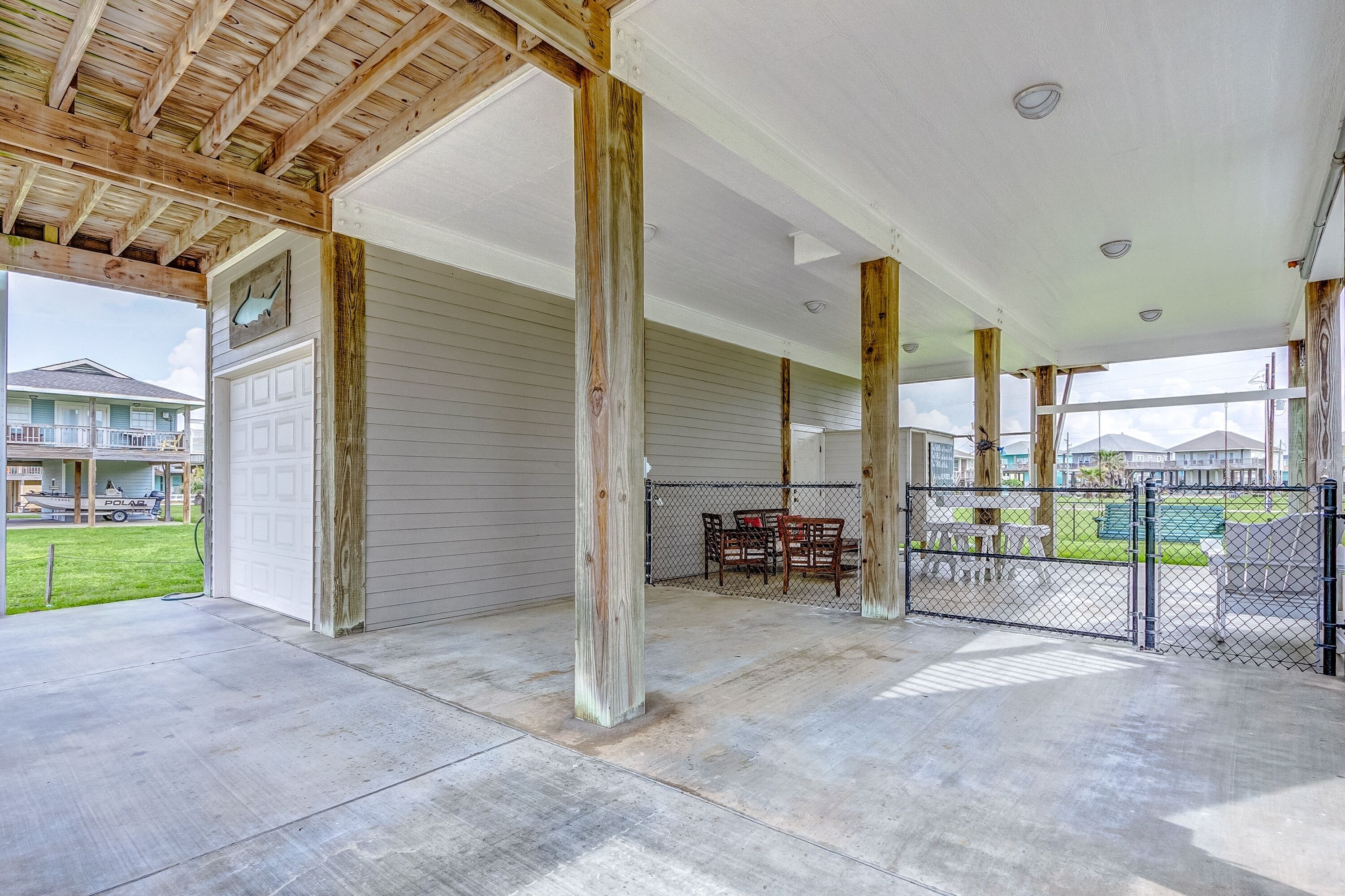A covered patio area with a concrete floor, wooden beams, and a view of a fenced backyard.