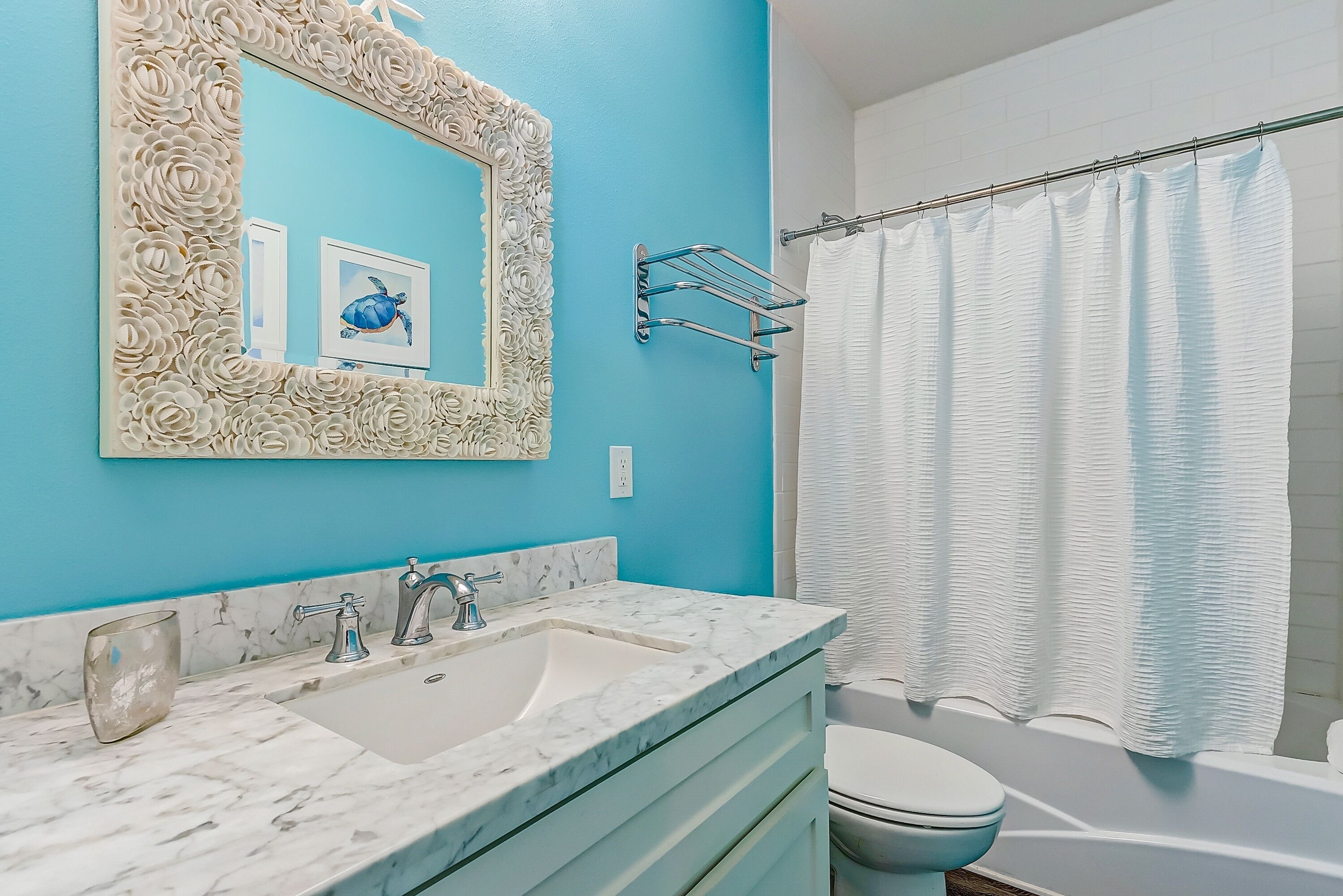 A bathroom with a marble sink, a white toilet, a shower with a white curtain, and a mirror with a floral frame.