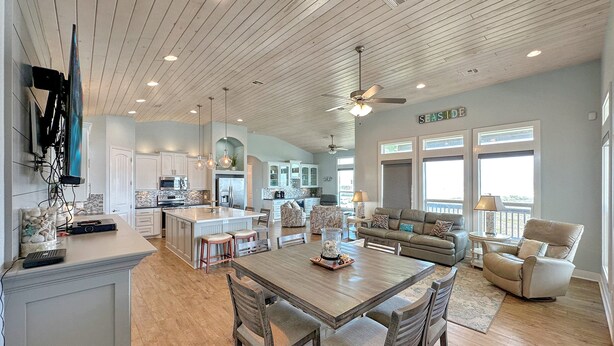A spacious kitchen with wooden cabinets, a central island, and a dining area with wooden chairs. - The Salty Mermaid 3 Bedroom Home (Port Bolivar)