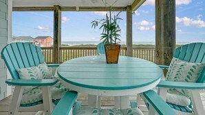 A covered patio with a round table and four chairs, a potted plant, and a view of the beach. - The Salty Mermaid 3 Bedroom Home (Port Bolivar)