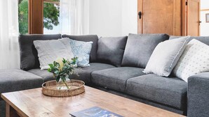 Een grijze bank met gekleurde kussens, een geweven mand met bloemen en een houten bijzettafeltje.