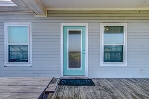 Une maison avec une porte de couleur turquoise, deux fenêtres équipées de stores et un porche en bois.