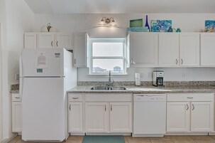 A kitchen with white cabinets, a refrigerator, a dishwasher, a window, and a coffee maker.