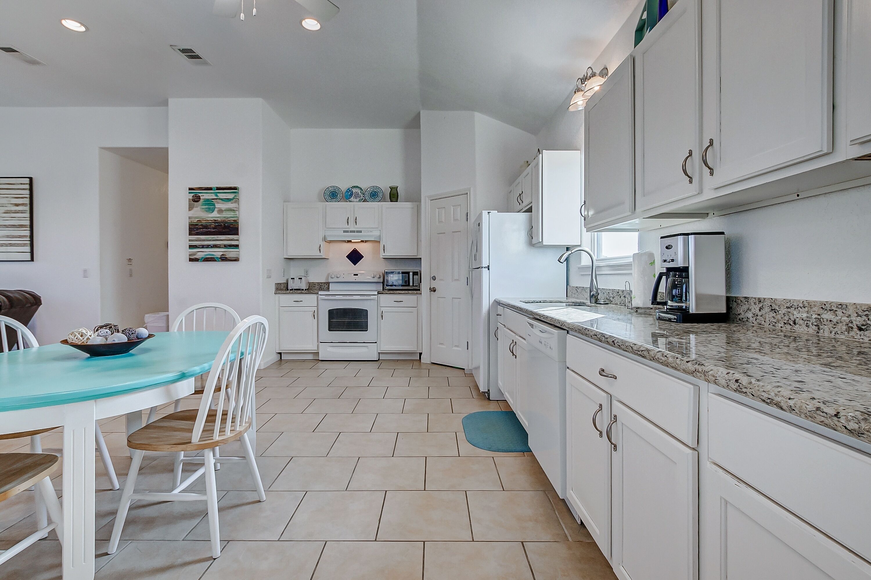 A modern kitchen with white cabinets, a granite countertop, and a dining area with a glass table and chairs.