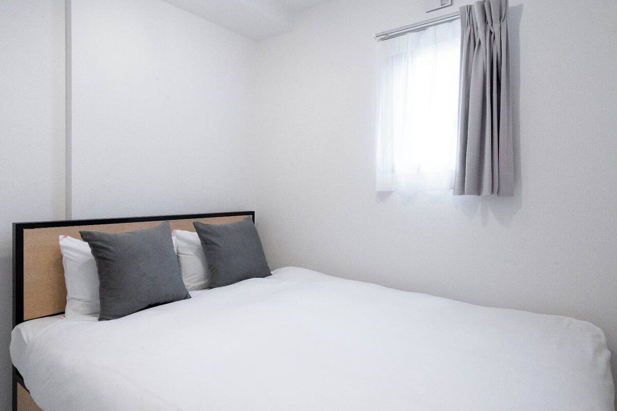 Un lit simple avec une tête de lit en bois, une literie blanche et trois oreillers dans des tons de gris et de blanc.