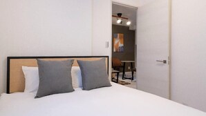 Een slaapkamer met een bed, twee kussens, een houten hoofdbord en een deur naar een badkamer.