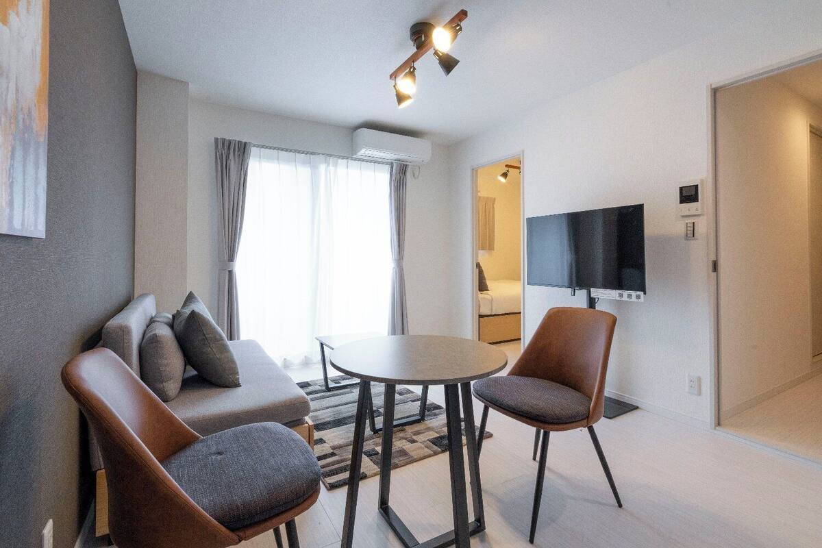 Une chambre d’hôtel moderne équipée d’un canapé, de deux fauteuils, d’une petite table, d’un téléviseur à écran plat et d’un luminaire au plafond.
