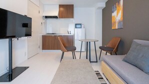 Een gezellig, compact ingerichte ruimte met een kitchenette, een bank, twee stoelen, een televisie en een schilderij aan de muur.