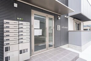 A building with a glass door entrance, numbered mailboxes, and a sign reading 'at Kyobashi.' - at Kyobashi  (Osaka)