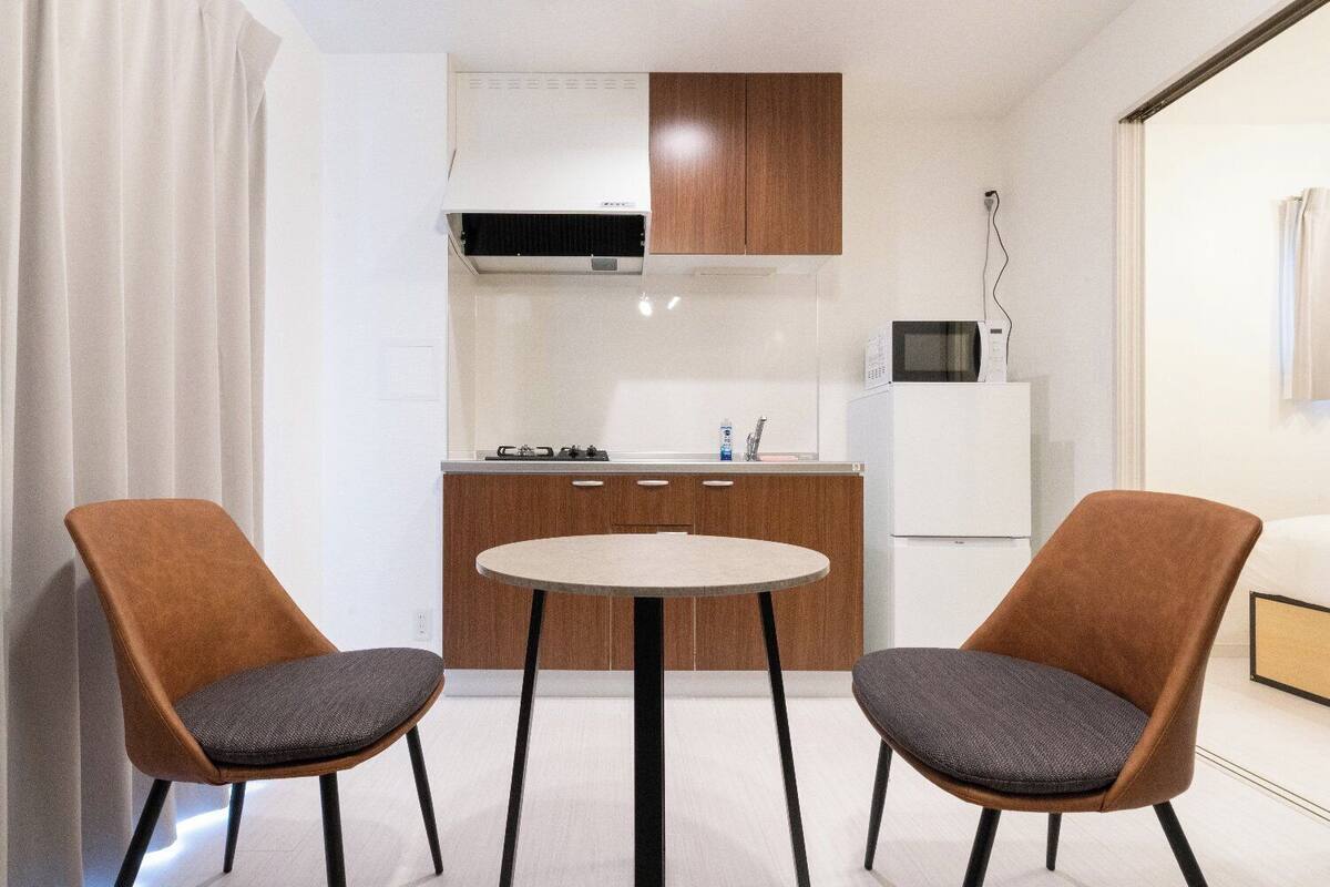 Une cuisine compacte équipée d’un four à micro-ondes, d’une cuisinière et d’un réfrigérateur. On y trouve deux chaises et une petite table ronde.