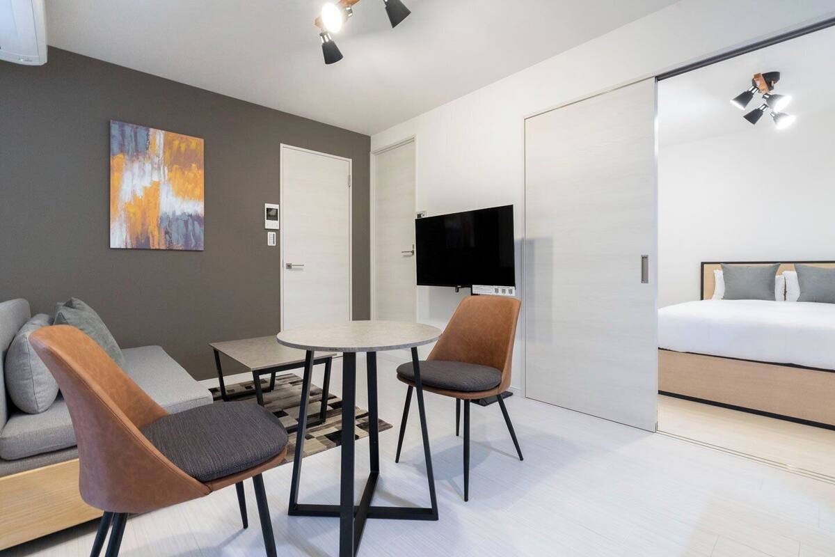 Une chambre d’hôtel moderne équipée d’un canapé, de deux fauteuils, d’une petite table, d’une télévision et d’un lit.