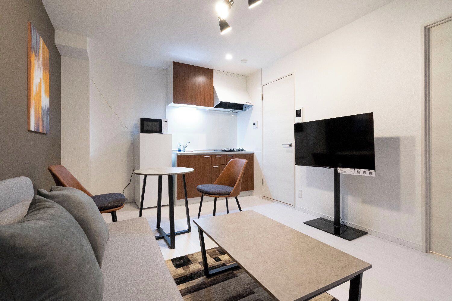 Een moderne woonkamer met een bank, salontafel en televisie. Er is een keukenhoek met een magnetron, fornuis en kastjes.
