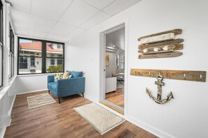 A modern living room with a blue sofa, wooden flooring, and a view through a large window. - Spacious 6BR - Sleeps 18| Beach Gear | Deck | BBQ (Ventnor City)