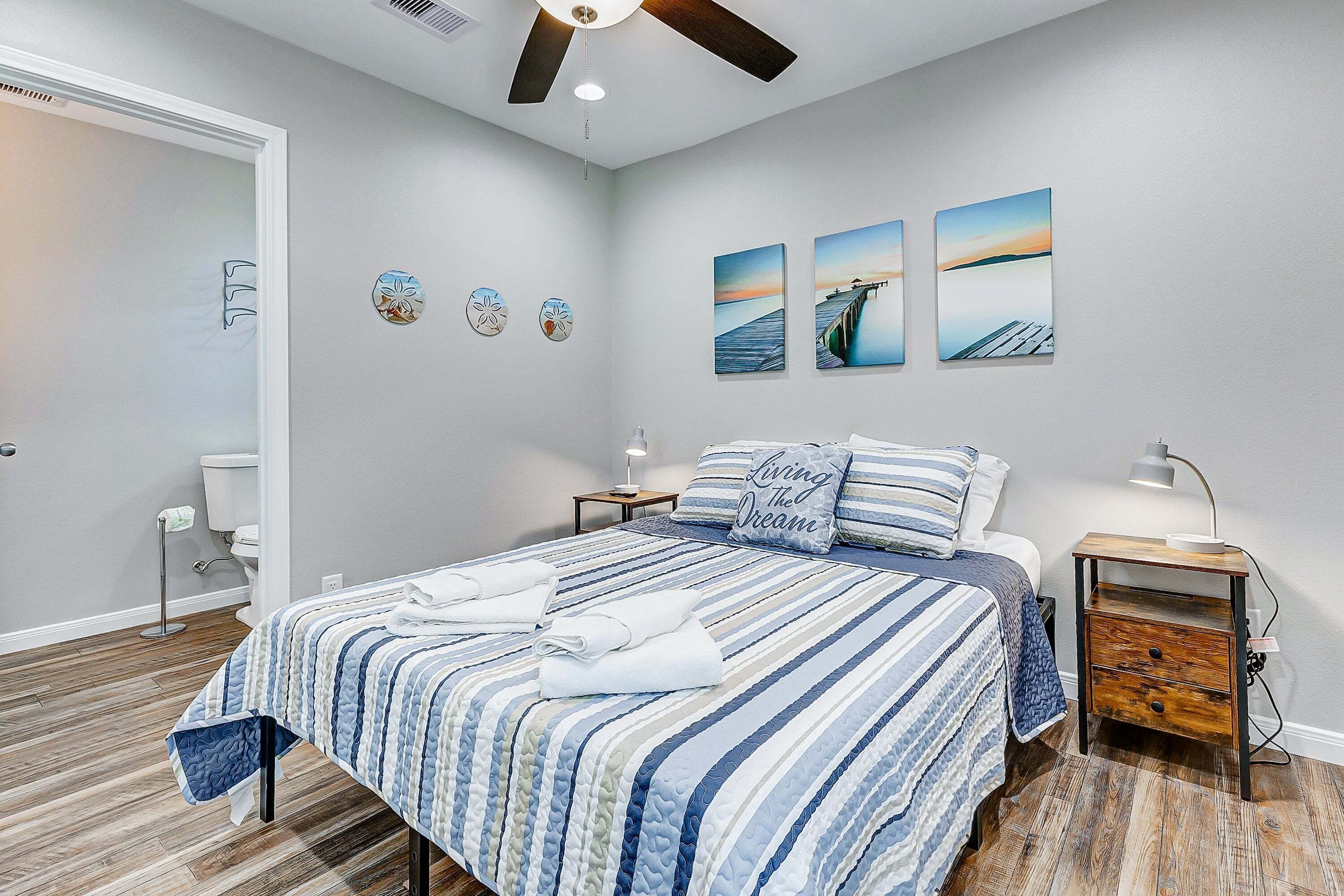 A bedroom with a bed, bedside tables, a nightstand, a ceiling fan, and artwork on the wall.