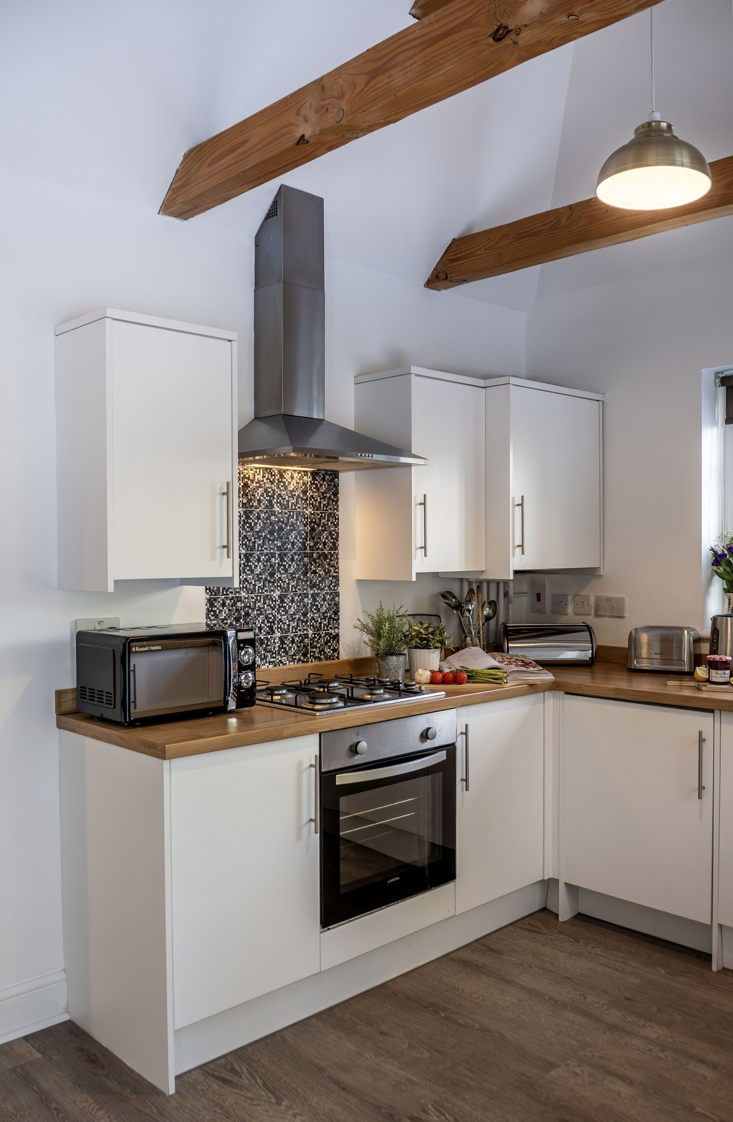 Une cuisine moderne avec des meubles blancs, un micro-ondes noir, une cuisinière à gaz et une hotte en acier inoxydable.